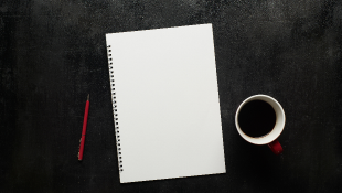 Coffee cup next to notebook on desk