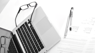 Glasses and Pen lying next to laptop